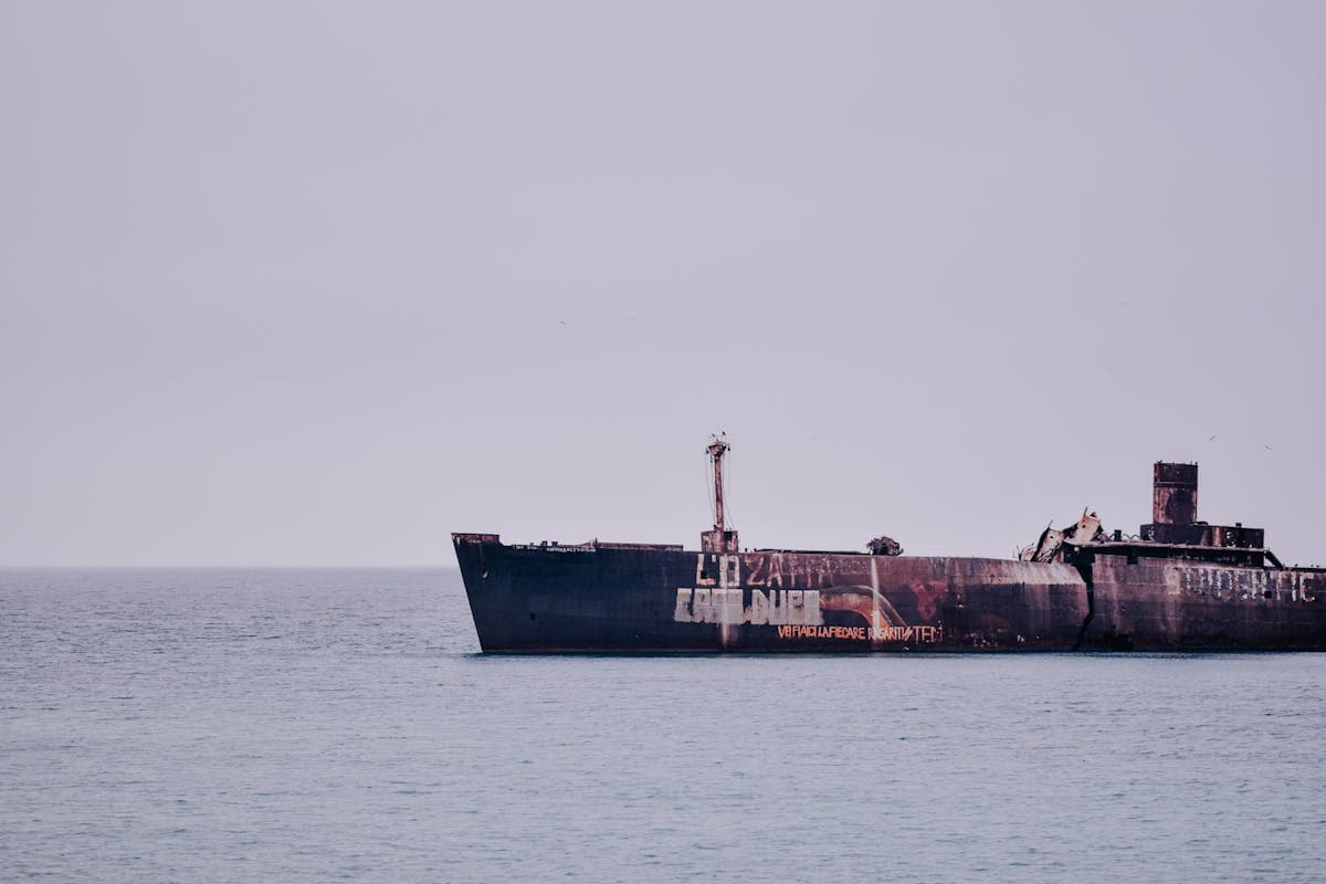 Weathered shipwreck resting in calm ocean waters under a clear sky, symbolizing the fate of abandoned vessels
