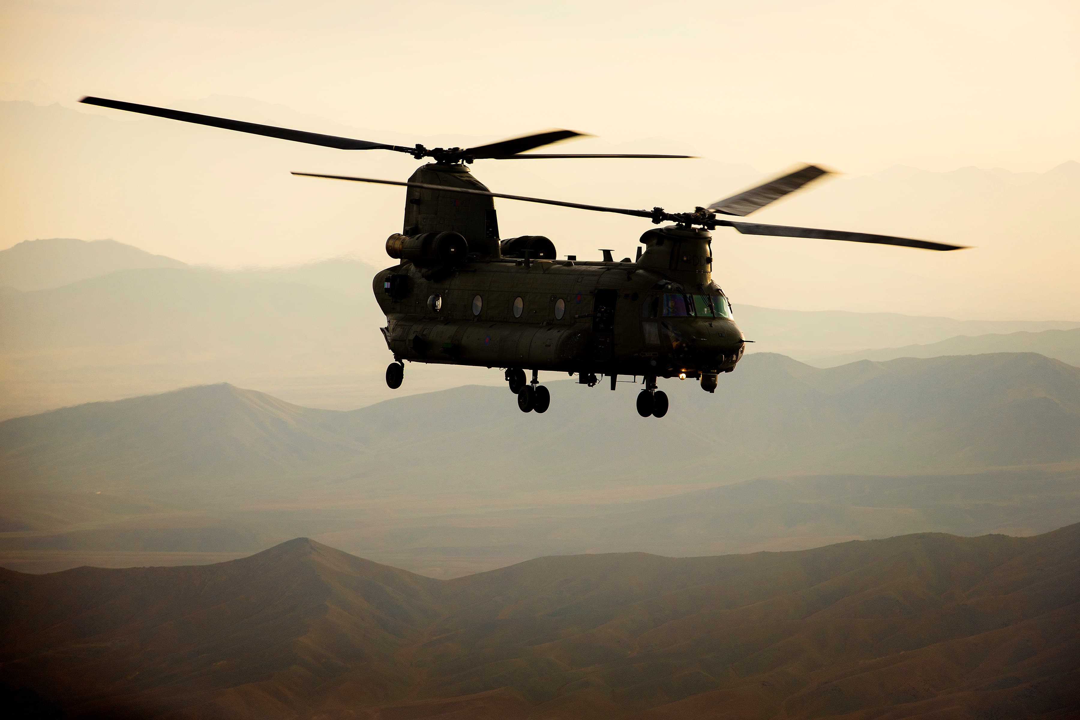 A tandem-rotor Chinook helicopter silhouetted against a hazy sky