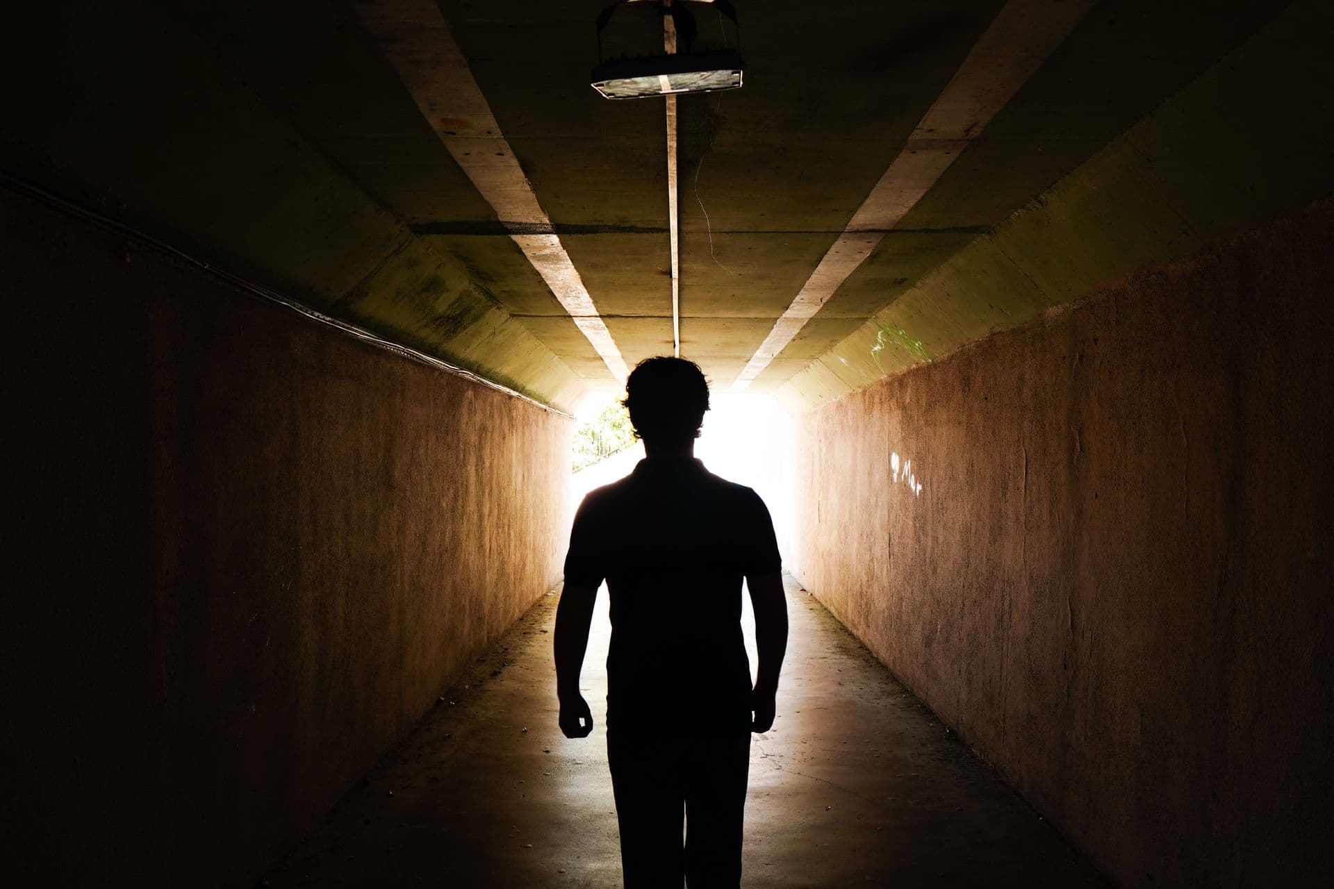 A lone silhouette walking toward a bright light at the end of a dark tunnel