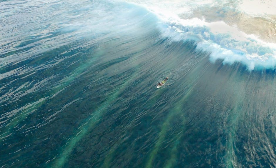 Aerial view of turquoise ocean waves and a tiny figure in the vast water