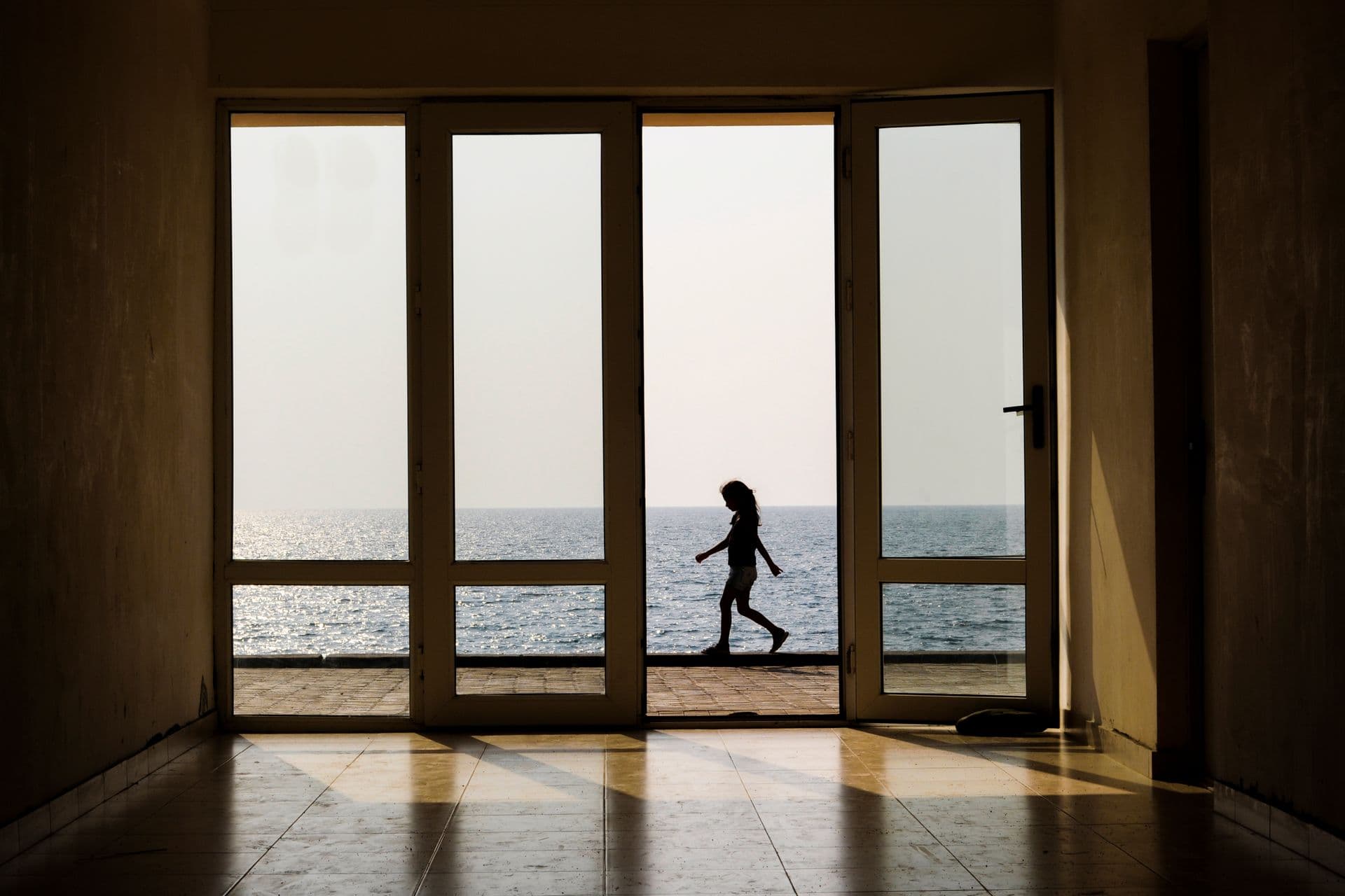 The silhouette of a child seen through a doorway, walking past a bright sea horizon