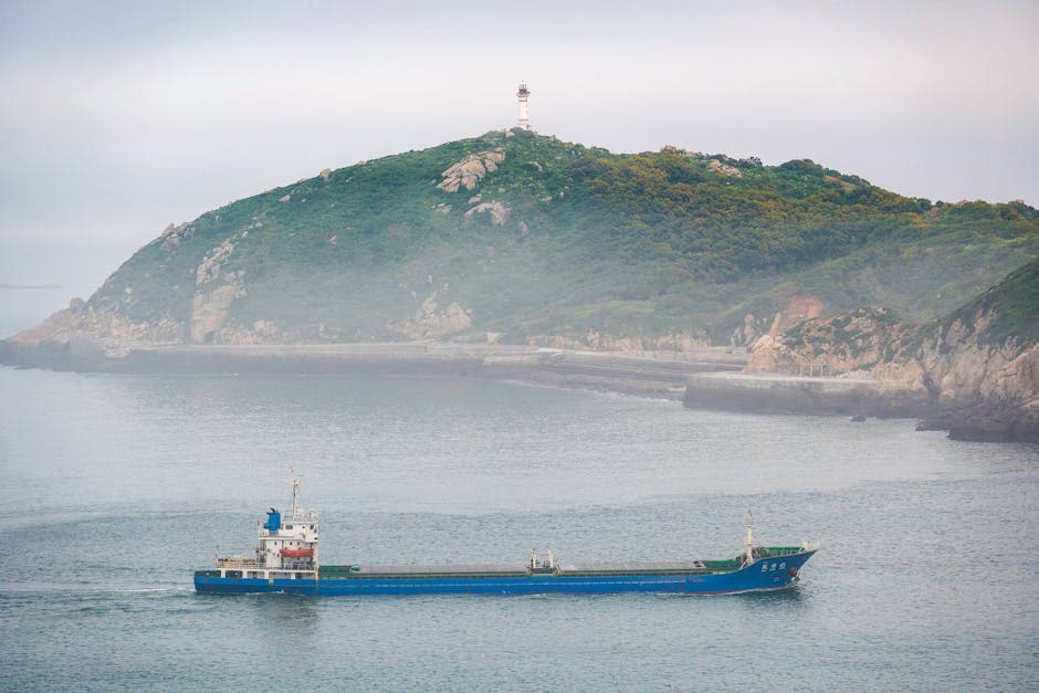 Cargo ship sailing near a lush green island coastline under clear skies