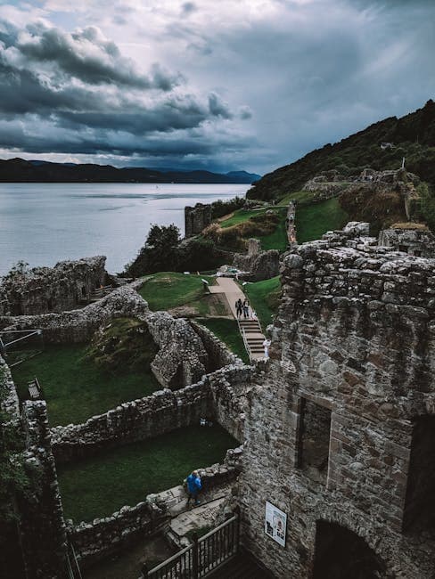Aerial view of Urquhart Castle ruins overlooking the serene Loch Ness under dramatic skies